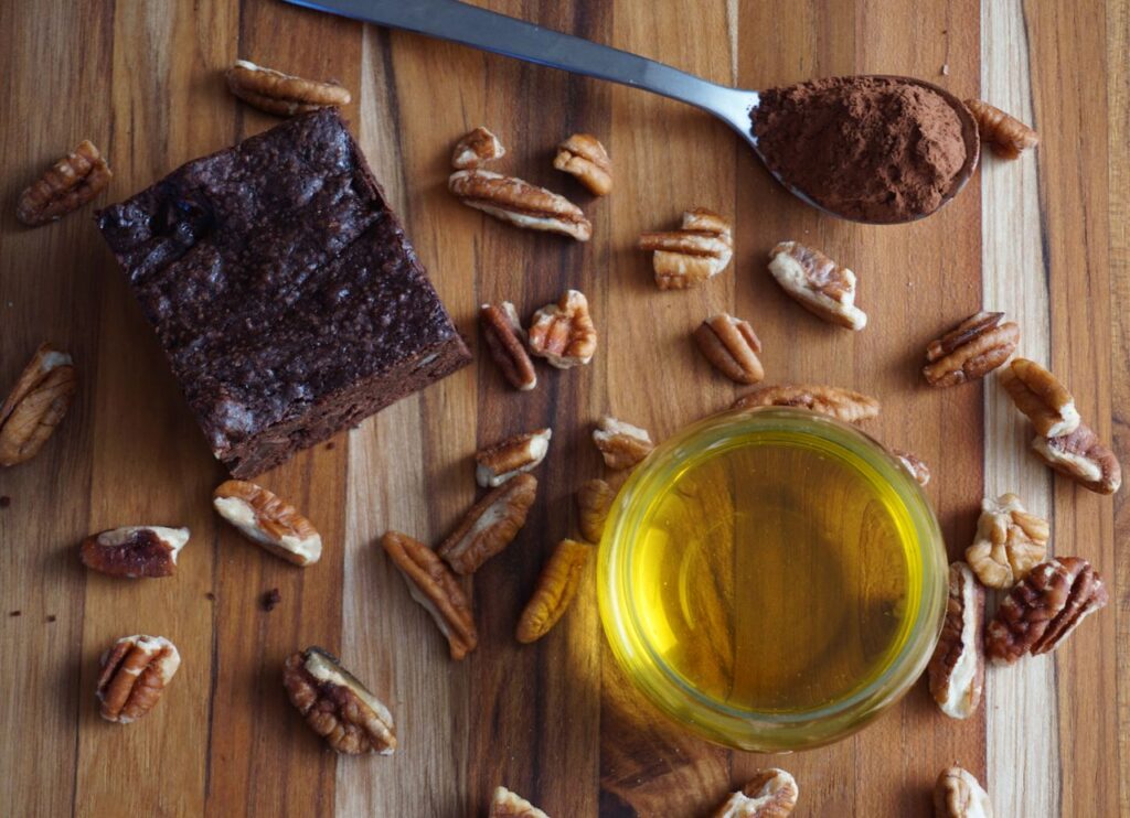 Flat lay of homemade chocolate brownie with pecans, cocoa, and oil. Perfect for baking visuals.