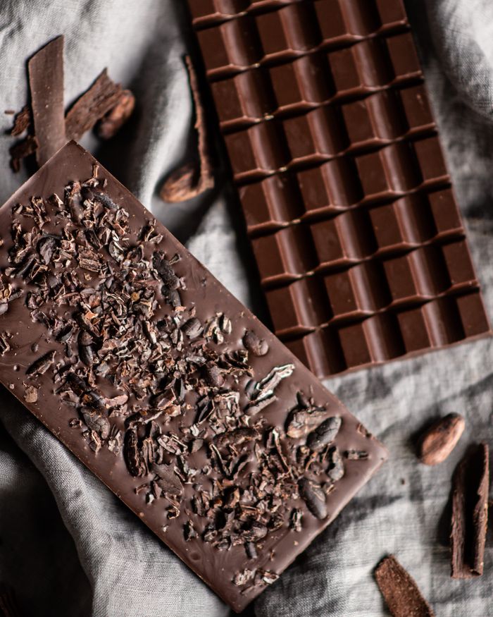 Tasty dark chocolate bar with cocoa and nut placed on white cloth with crumbs